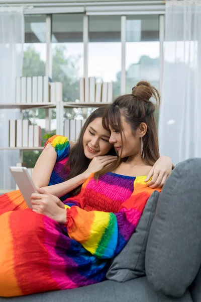 Young woman with tablet sitting on sofa in living room. Happy smiling asian woman using digital tablet. Young couple shopping online on the sofa in their living room at home.