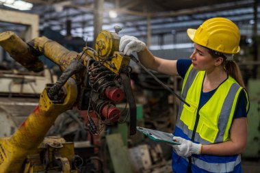 Engineer holding clipboard with the machine works. Female caucasian industrial worker in factory. Staff or technicians are checking the operation of the old machine.