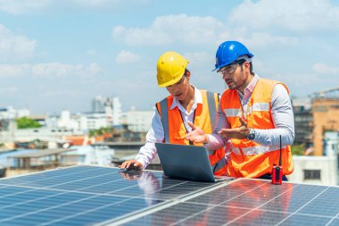 Mühendisler dizüstü bilgisayarla güneş enerjisi santrali projesini tartışıyorlar. Güneş paneli teknisyeni çatıda. Mühendis ve genç teknisyen fabrikanın çatısına güneş panelleri kuruyor..