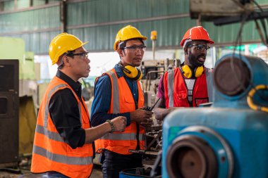 Metal işçisi stajyere makinede öğretiyor. Fabrikada güvenlik üniforması giyen mühendisler..