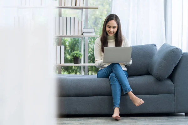 Asian woman sitting on sofa. Young Asian woman working with a laptop computer sitting on the cozy sofa.