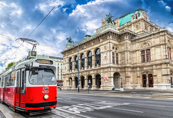 Vienna, Austria - October 06, 2021: imposing and luxurious arched faade of the Vienna Opera House and the old traditional red tram. Popular tourist attraction in Austria. Ancient baroque architecture