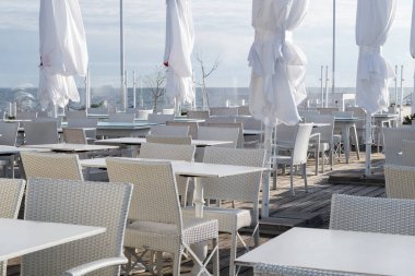 Güneşli bir sahil kenarındaki bir kafede masa ve sandalyeler.