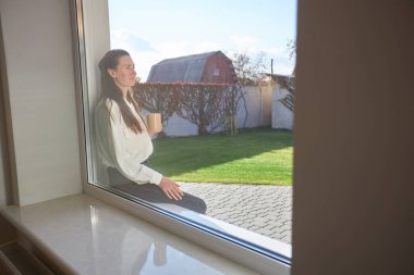 Kadın kahve içerken arka bahçesinde, pencerenin yanında dinleniyor.