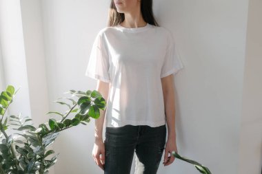 Logonuz için yeri olan beyaz, boş tişört giyen bir kadın. Kapalı mekanda modellik veya tasarım yapın.