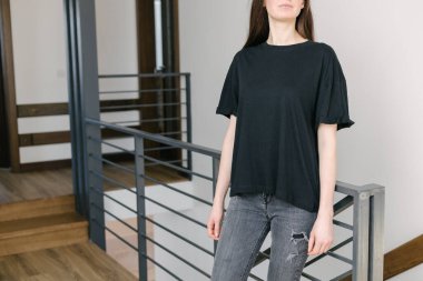 Logonuz için yeri olan siyah, boş tişört giyen bir kadın. Kapalı mekanda modellik veya tasarım yapın.