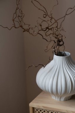 İçi beyaz vazo ahşap masa ve dallarla dolu.