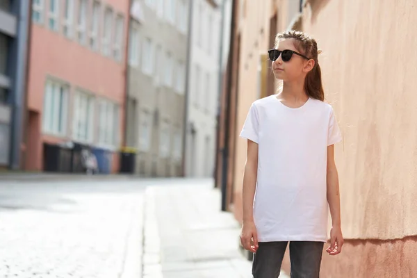 あなたのロゴのためのスペースが付いている白いTシャツを身に着けているか 都市部で外にモックアップ子供の女の子 — ストック写真