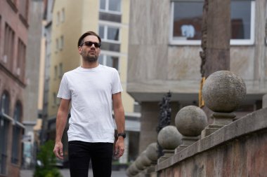 Hippi gibi yakışıklı bir erkek modelin üzerinde beyaz boş tişört. Logonuz ya da gelişigüzel tasarlanmış bir şehir tarzı.