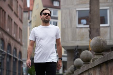 Hippi gibi yakışıklı bir erkek modelin üzerinde beyaz boş tişört. Logonuz ya da gelişigüzel tasarlanmış bir şehir tarzı.