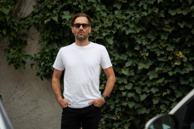 Hippi gibi yakışıklı bir erkek modelin üzerinde beyaz boş tişört. Logonuz ya da gelişigüzel tasarlanmış bir şehir tarzı.