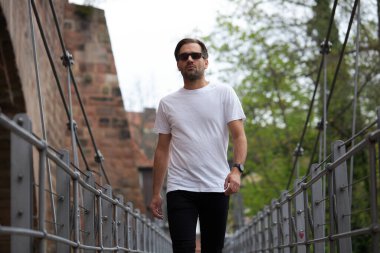 Hippi gibi yakışıklı bir erkek modelin üzerinde beyaz boş tişört. Logonuz ya da gelişigüzel tasarlanmış bir şehir tarzı.