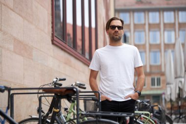 Hippi gibi yakışıklı bir erkek modelin üzerinde beyaz boş tişört. Logonuz ya da gelişigüzel tasarlanmış bir şehir tarzı.