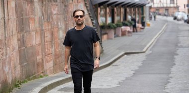 Hippi gibi yakışıklı bir erkek modelin üzerinde siyah boş tişört. Logo ya da şehir tarzı tasarım için yeri var.