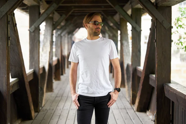 Hippi gibi yakışıklı bir erkek modelin üzerinde beyaz boş tişört. Logonuz ya da gelişigüzel tasarlanmış bir şehir tarzı.