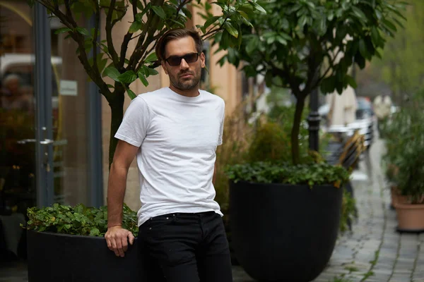 Hippi gibi yakışıklı bir erkek modelin üzerinde beyaz boş tişört. Logonuz ya da gelişigüzel tasarlanmış bir şehir tarzı.