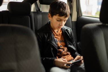 Arka koltukta akıllı telefon kullanan arabadaki genç çocuk, dikey fotoğraf