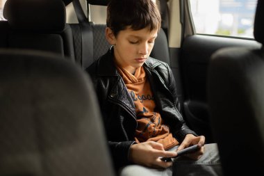 Arka koltukta akıllı telefon kullanan arabadaki genç çocuk, dikey fotoğraf
