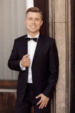 Beyaz gömlekli, papyonlu, kendine yeten adam, işadamı ya da damat portresi, binanın arka planına bakıyor.. 