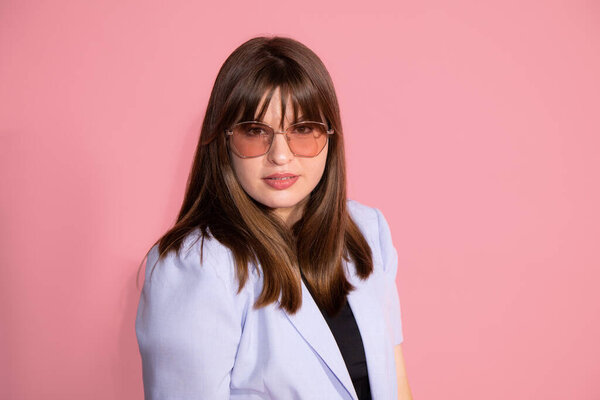 Young woman 25 years with bangs of dark hair in pink sunglasses. Photo on background in studio, looks at camera. High quality photo