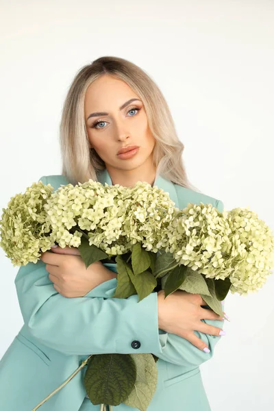 腕のアジサイの花の腕とミントグリーンのパンツに長い髪の若い美しいブロンドの女性 肖像画 — ストック写真