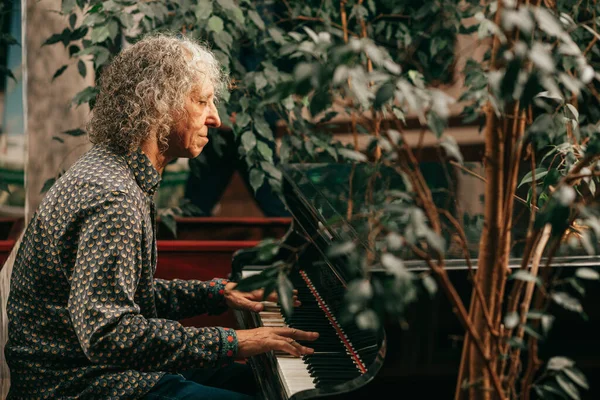 長髪の白髪の老人の肖像画は ピアノに座って音楽を演奏し ホテル サイドビューで快適な夜を楽しんでいます ライフスタイル写真 — ストック写真