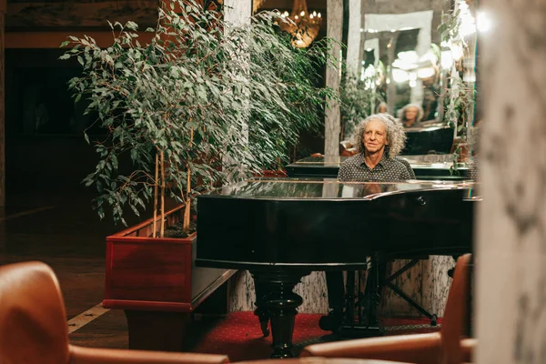 70歳の男性の写真遠くからホテルのロビーで壮大なピアノを演奏 灰色の巻き毛 — ストック写真