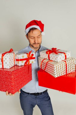 Noel Baba şapkalı acımasız iş adamı elinde bir sürü hediye kutusu tutuyor. Gri arka planda stüdyo çekimi, Noel konsepti.