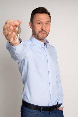 İş adamının sana evin anahtarlarını verdiği fotoğraf, emlakçının anahtar verdiği fotoğraf, stüdyo fotoğrafı, gri arka plan, ev anahtarı tutan neşeli şirket adamı.. 