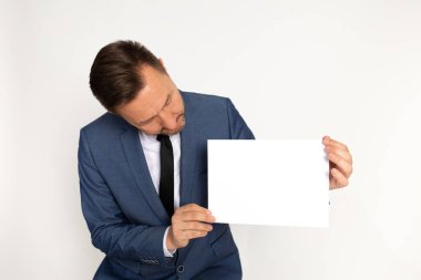 Çekici bir adam, iş adamı takım elbiseli ve kravatlı. Yazı için beyaz bir sayfa üzerine eğilmiş. Kopya alanı, stüdyo çekimi, beyaz arkaplan. İşaretin için.