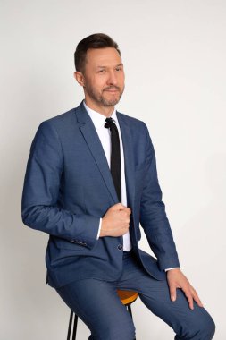 Stüdyoda sandalyede oturan, kendine güvenen ve cana yakın görünen, kravatlı, yakışıklı beyaz bir ofis çalışanının portresi. İş konsepti. Beyaz arka plan. Stüdyo çekimi