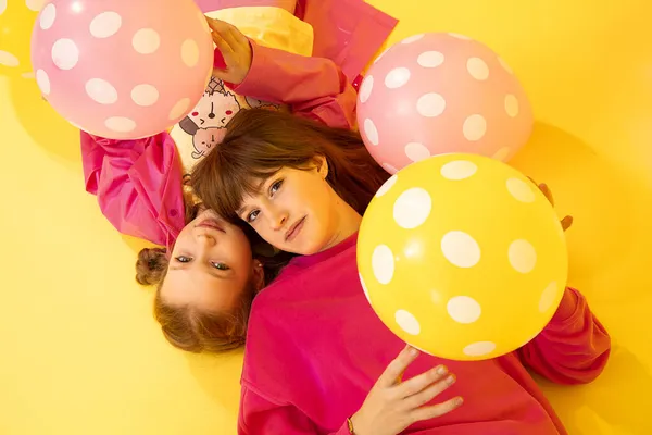 Dziewczęce Siostry Leżą Żółtym Tle Studiu Patrząc Kamerę Wśród Balonów — Zdjęcie stockowe