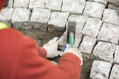 İşçi tuğlalardan kaldırım döşedi. Elinde çekiçle, omuz manzarasının üstünden.. 