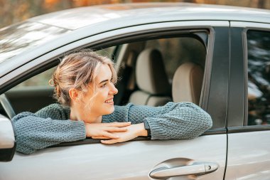 Genç ve güzel sarışın bir kadının fotoğrafı açık arabanın camından dışarı baktı, neşeyle gülümsedi ve etrafına baktı. Mutlu yolculuklar, rahatlama anı, aktif yaşam tarzı. Yüksek kalite fotoğraf