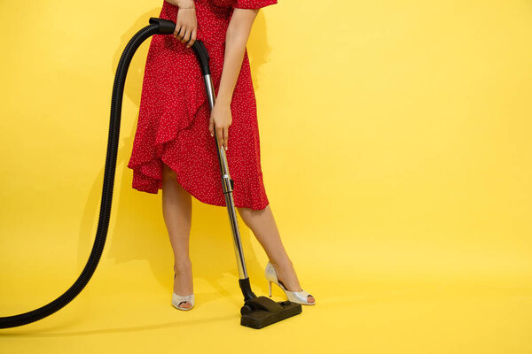 Photo of slender beautiful unrecognizable woman in red dress on yellow background holds vacuum cleaner in hands. concept of cleaning in offices, at home. Easy cleaning, beautiful legs in heels.