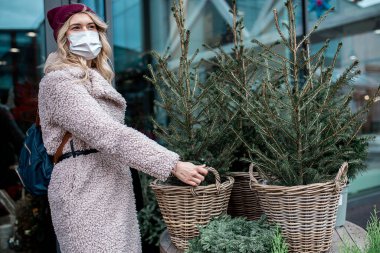  Sahte kürklü ve şapkalı bir kadın, çiçekçide hasır tencerede küçük bir Noel ağacını asıyor.