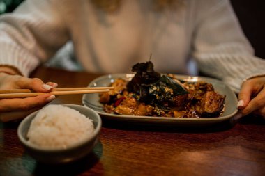 Asya restoranında baharatlı sebzeleri yerken elinde yemek çubukları tutan tanınmamış bir kadın. Yemek zamanı, lezzetli yemekler, ahşap masa..