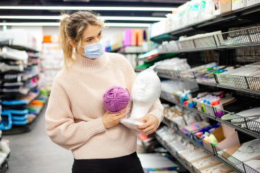 Yaratıcı bölümündeki maskeli çekici sarışın elinde alçı büstü ve iplikler ve çeşitli çalışmalar tutuyor. Salgın hastalık alışverişi. El işleri ve yaratıcılık. Yeni normal kavram .