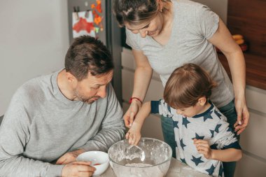 4-5 yaşlarında şirin bir çocuk ve güzel bir anne-baba mutfakta kurabiye pişirirken mutlular. Anne, baba ve oğul birlikte yemek partisi yapıp, mutlu saatler geçiriyorlar.