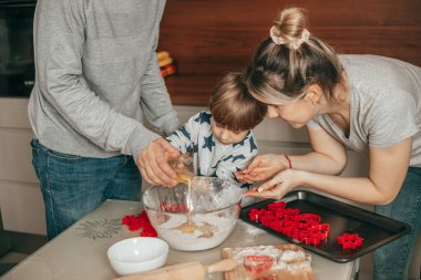 Mutlu bir aile, ev mutfağında birlikte yemek pişirirken, takım çalışması, yemek pişirirken, baba, anne, çocuk, beraberlik, kurabiye kesiciler, yardım eli, 4-5 yaşındaki çocuk.