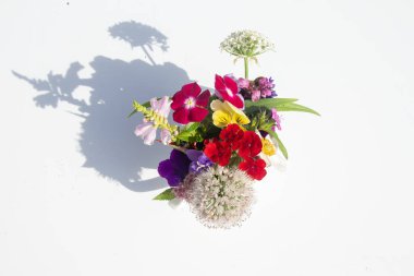 Beyaz masanın üzerinde duran renkli güzel yaz çiçekleriyle dolu bir vazo. Güneş ışığı, ışık ve gölge oyunu. Yukarıdan görüntüle.