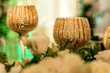 Beyaz çiçeklerle çevrili lüks altın şarap kadehleri genellikle yeni evliler için masa dekorasyonudur. Çiçek aranjmanı. Şenlik etkinlikleri düzenliyorum. Ziyafetlerin dekorasyonu ve tasarımı. 