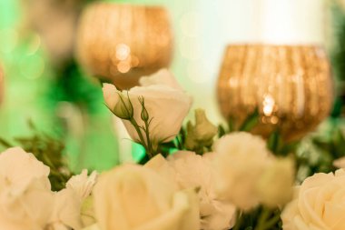 Odaklanmamış altın şarap kadehlerinin arkasındaki narin beyaz güller yeni evliler için masa süsü olarak kullanılıyor. Çiçek aranjmanı. Düğün çiçekçisi olarak. Şenlik etkinlikleri düzenliyorum. Ziyafetlerin dekorasyonu.