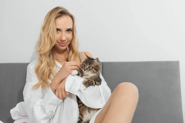 Portrait de jeune femme blonde tenant un chat brun blanc et noir regardant la main. Nourrir le chat. Câlin doucement chaton — Photo