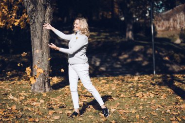 Güzel görünüşlü orta yaşlı, uzun dalgalı sarı saçlı, gri yaka kazaklı, sarı akçaağaç yapraklı bir kadın..