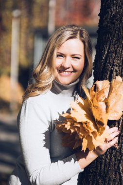 Dalgalı, sarı saçlı, yuvarlak boyunlu güzel bir kadın. Ağaçlara sarılmış yapraklardan bir buket tutuyor.