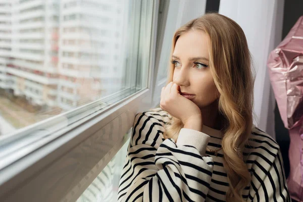 Portré töprengő szőke, elég szomorú depressziós nő az ablakpárkányon, távolra néz. Magányos, fáradt, elszigetelt. Közelről. — Stock Fotó