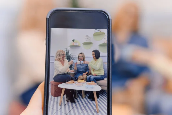 Kobiece ręce robiące zdjęcia na smartfonie trzech kobiet jedzą razem ciasta. Rodzina je razem posiłek — Zdjęcie stockowe