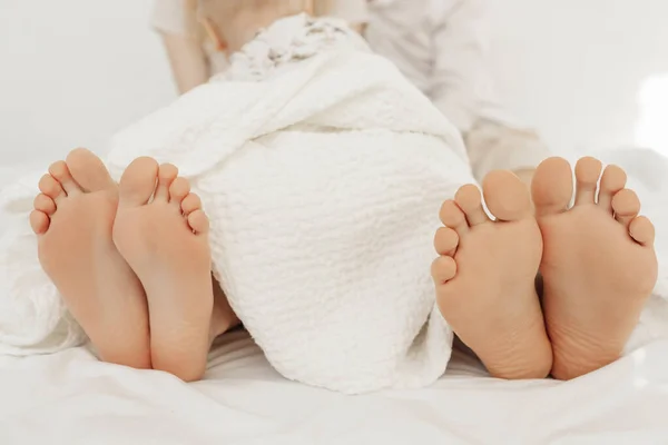 小さな赤ちゃんの幼児が横たわっている家族の裸の足の終わり、白い綿の毛布で覆われたベッドの上で休んで. — ストック写真