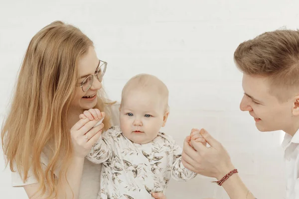 Портрет молодої щасливої усміхненої красивої сім'ї з хворобливим блакитнооким малюком у білому одязі, що сидить . — стокове фото